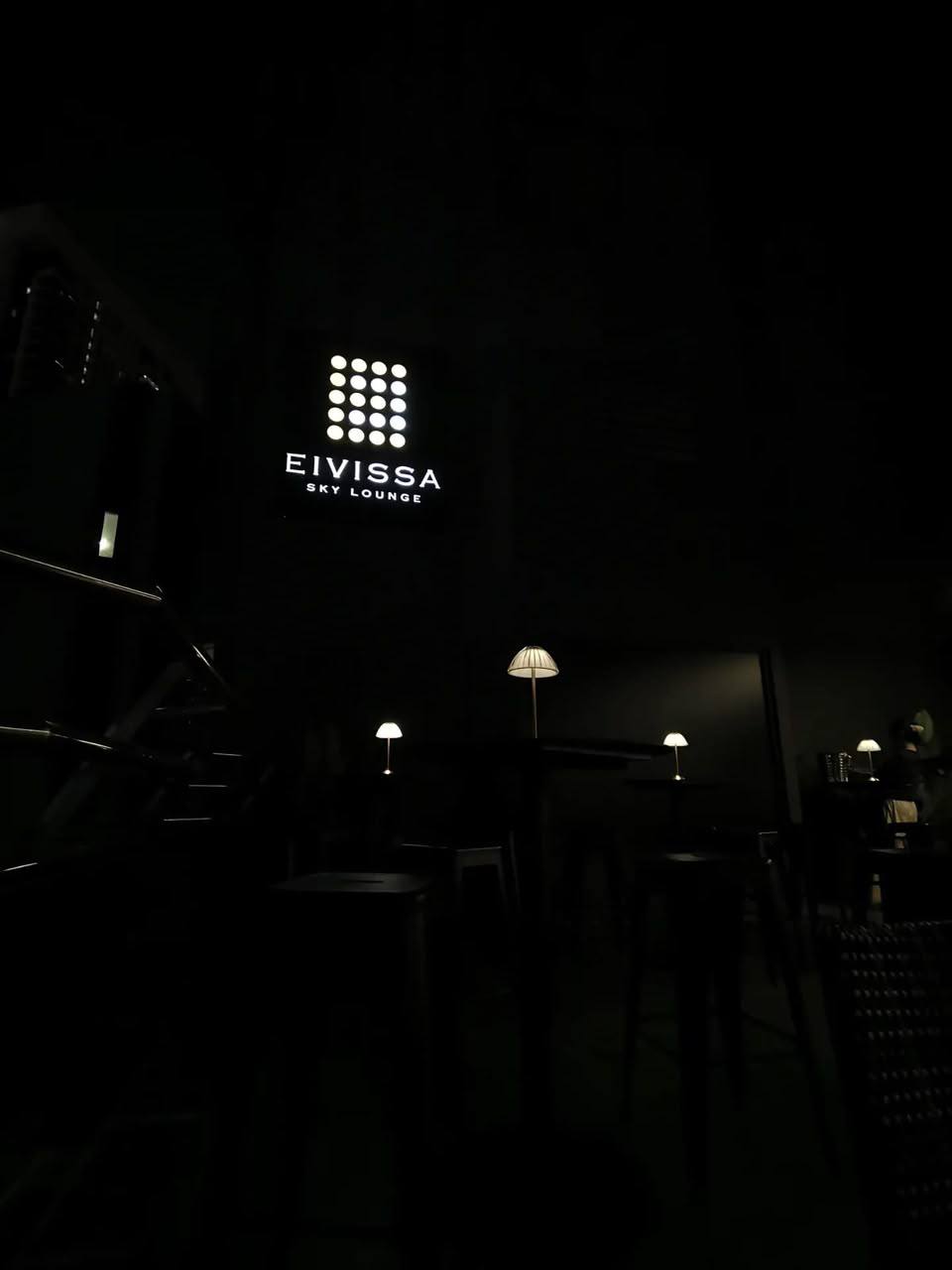 Eivissa Sky Lounge — the illuminated dot-grid sign glowing on a dark wall above lamp-lit cocktail tables.